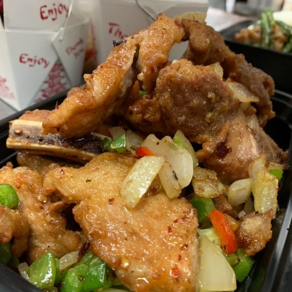 Chow n Joy's fried pork ribs with onions and peppers, with takeout boxes in the background.