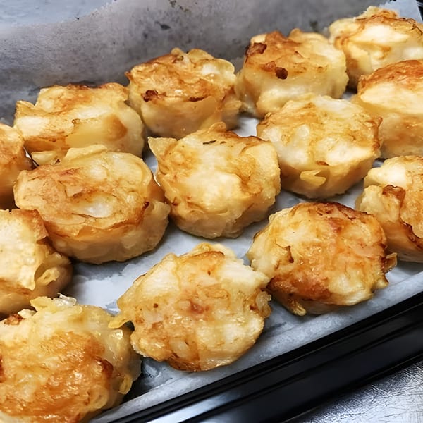 Close-up of golden-brown fried dumplings, likely Shumai, arranged in a tray with parchment paper.