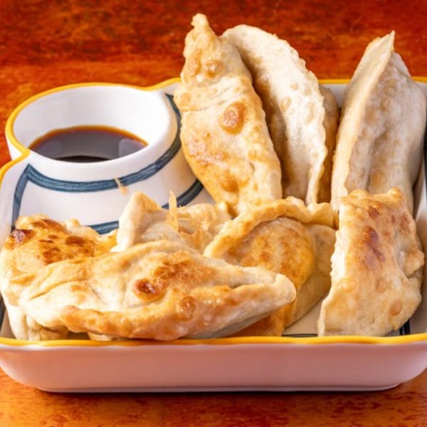 A plate of golden-brown fried dumplings with a side of soy sauce, from Chow n Joy.