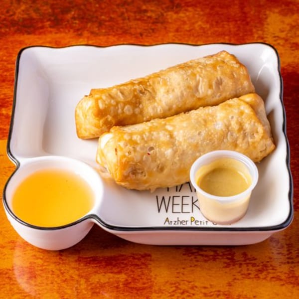 Two golden-brown egg rolls with two dipping sauces on a white rectangular plate.