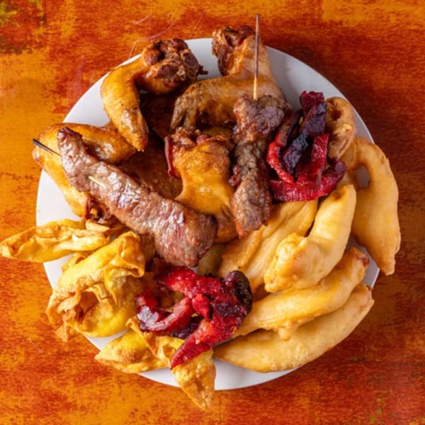 A white plate piled high with various Chinese appetizers, including chicken wings, beef skewers, and wontons.